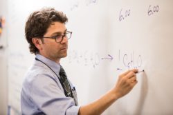 A chemistry teacher writes chemistry equations on the board